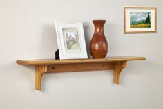 a wooden shelf with two pictures and a vase on it