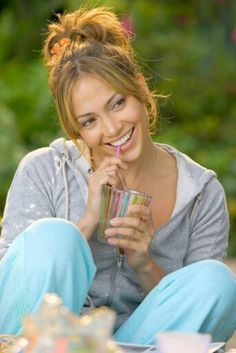 a woman sitting on the ground holding a drink and looking at the camera while smiling