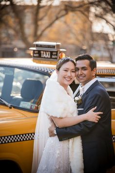 a bride and groom standing in front of a taxi cab with their arms around each other