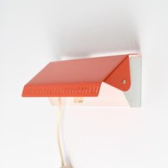 an orange and white wall light with a red shade on it's head hanging from the ceiling