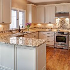 a large kitchen with white cabinets and granite counter tops on the island in front of an oven