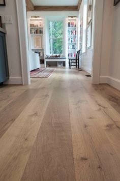 an empty hallway with wood floors and white walls, leading to a living room area