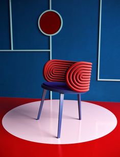 a red and blue chair sitting on top of a white circle in front of a blue wall