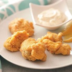 some fried food on a white plate next to a lemon wedge and dipping sauce in a small bowl