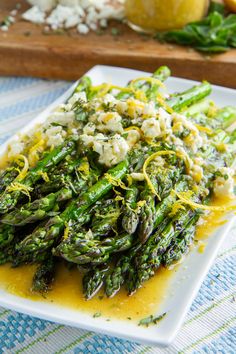 asparagus with feta cheese and lemon sauce on a white plate next to an orange