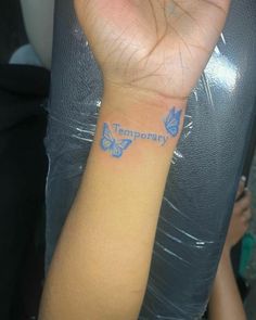 a woman's arm with blue butterflies on it, and the word temporary written on her wrist