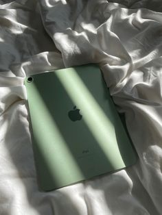 an apple ipad sitting on top of a white sheet covered bed with the cover pulled down