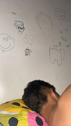 a man sleeping on top of a bed next to a wall with drawings on it