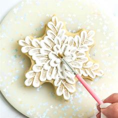 a cookie decorated like a snowflake being held by a person with a paintbrush