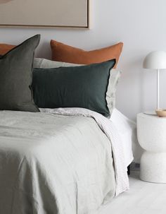 a white bed topped with lots of pillows next to a night stand and table lamp