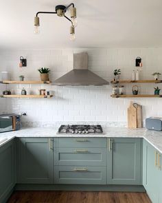 a kitchen with green cabinets and white subway backsplash, wood flooring and open shelving