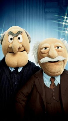 two puppets dressed in business attire stand next to each other, one with a moustache on his face