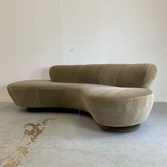 a curved couch sitting on top of a cement floor next to a white wall in an empty room