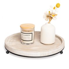 a white vase with flowers and a candle on a wooden tray next to a jar