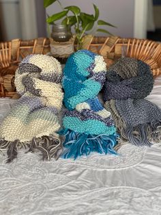 three knitted scarves sitting on top of a bed next to a potted plant