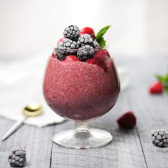 a glass filled with raspberry and blackberries on top of a wooden table