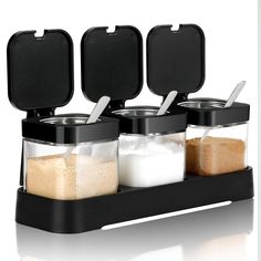 three containers with spoons and salt in them on a black tray next to each other