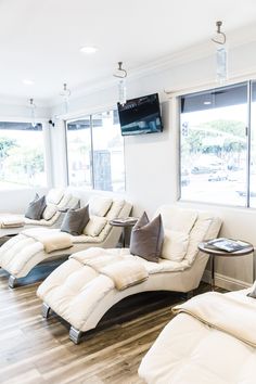 a living room filled with lots of white couches next to a tv mounted on the wall