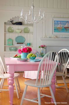 a pink table and chairs in a room with white walls, wood flooring and a chandelier hanging from the ceiling