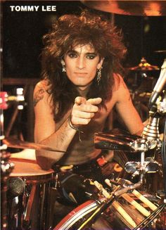 a man with long hair sitting in front of a drum kit