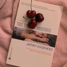 a book with two cherries on it laying on a pink blanket next to a pair of scissors