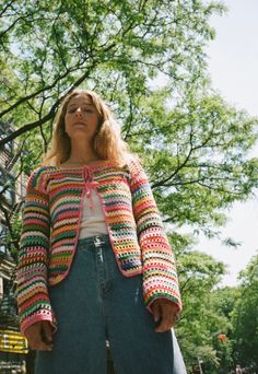 a woman standing in front of a tree with her eyes closed wearing a colorful crocheted jacket