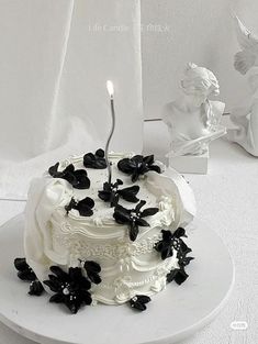 a white cake with black flowers and a single candle