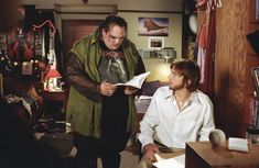 two men standing in a living room looking at papers