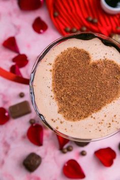 a heart shaped drink in a glass on a table with chocolates and hearts around it