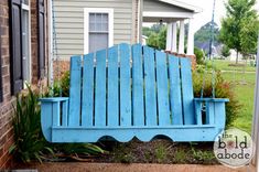 a blue wooden bench sitting in front of a house next to a green planter