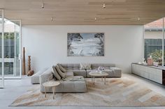 a modern living room with white walls and wood ceilinging, large sectional sofa set on top of a beige area rug