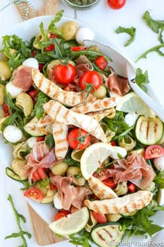 a salad with meat, tomatoes and cucumbers on a white plate next to a knife