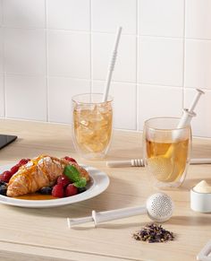 a white plate topped with fruit and pastry next to a glass of tea on a table