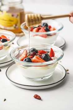 a person pouring honey into a bowl of fruit salad