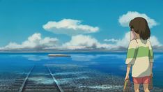 a girl standing on train tracks looking out at the water and clouds in the sky