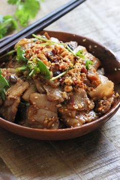 a brown bowl filled with meat and vegetables next to chopsticks on a table