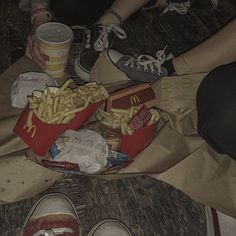 two people are sitting on the floor eating french fries and soda while one person is holding a drink