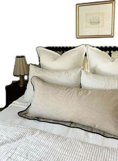 a bed with white and black pillows on top of it next to a framed painting