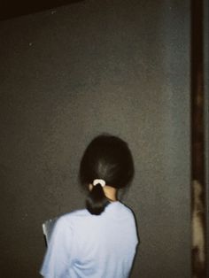 a woman standing in front of a wall with her back to the camera and looking down