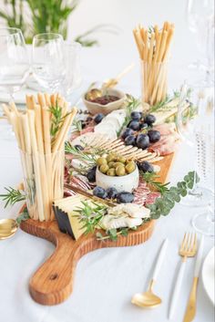 an assortment of cheeses, olives and bread sticks on a wooden platter