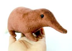 a hand holding a small stuffed animal in it's right hand, against a white background