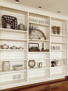 an open bookcase with many items on it in a room that has wood floors and white walls