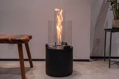 a large black cylinder with flames in it on the floor next to a wooden stool