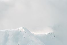 a snowboarder is in mid air on a snowy mountain top with clouds overhead