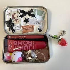 an open tin with various items in it and a strawberry on the table next to it