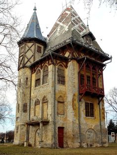 an old building with two towers on the top and one at the bottom, in front of some bare trees