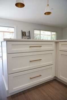 an empty kitchen with white cabinets and gold pulls on the countertop, along with two pendant lights