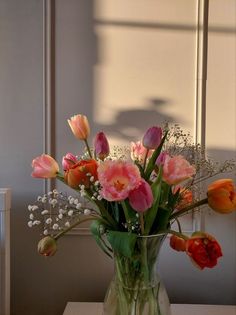 a vase filled with pink and orange flowers on top of a table next to a window