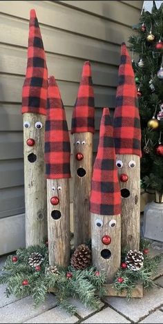 three wooden logs with faces painted on them and pine cones in front of a christmas tree