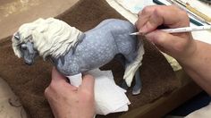 a person is painting a toy horse with white hair